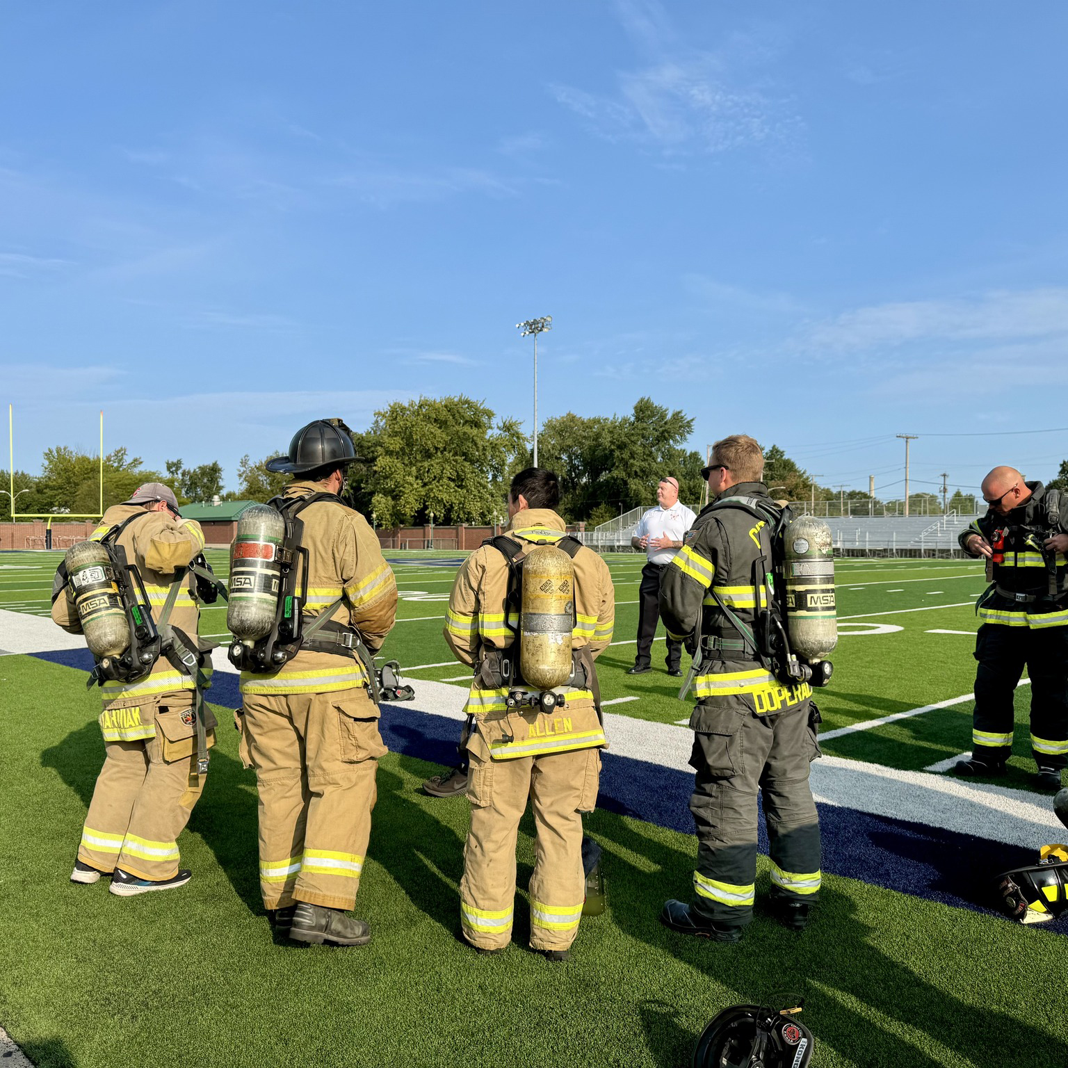 480770007_946301487683409_4430770283029159411_n-scaled Firefighters in SCBA gear participating in a training session on a football field with a chief speaking in the background